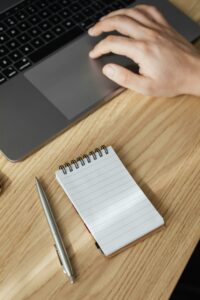 Crop man using touchpad on laptop and notebook with pen